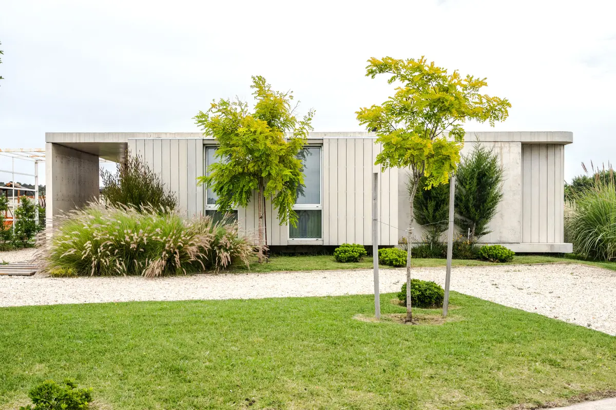 Casa moderna minimalista con fachada de hormigón blanco y madera, rodeada de césped y árboles — proyecto casa sr, por GARAGE arquitectura