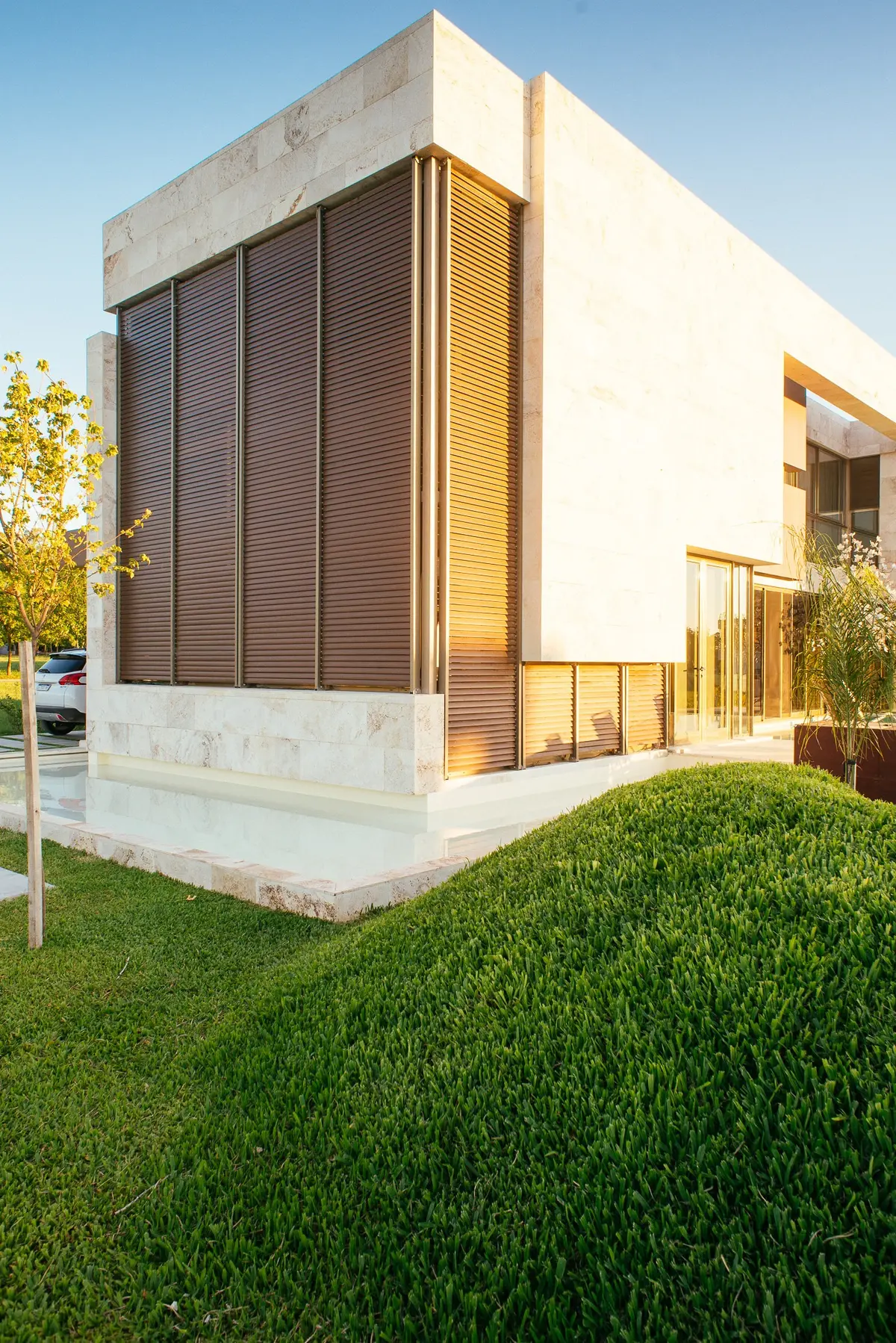 Fachada moderna con piedra, postigos y espejo de agua — proyecto Grand Bell 60, por Mercedes  klappenbach, en City Bell