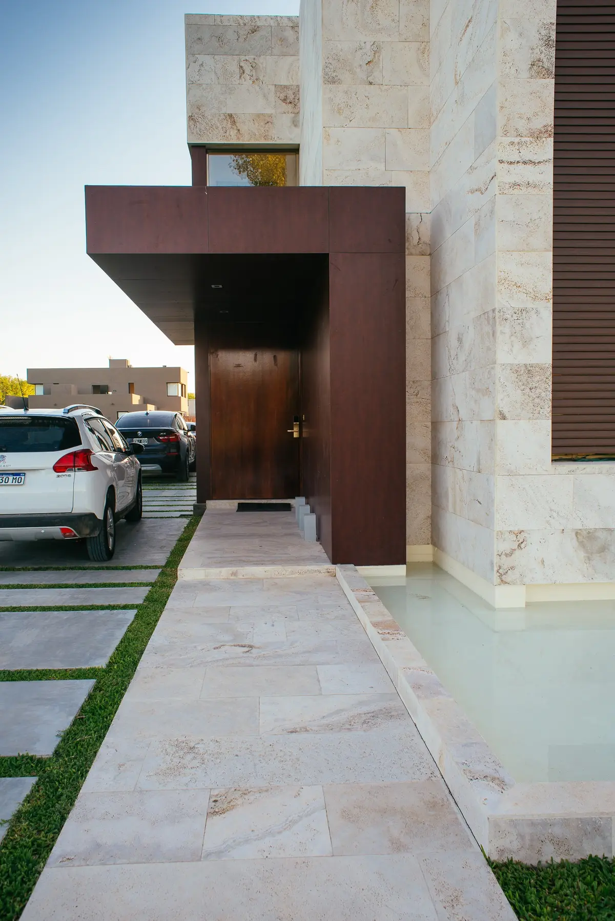 fachada moderna con piedra, madera y agua — proyecto Grand Bell 60, por Mercedes  klappenbach, en City Bell