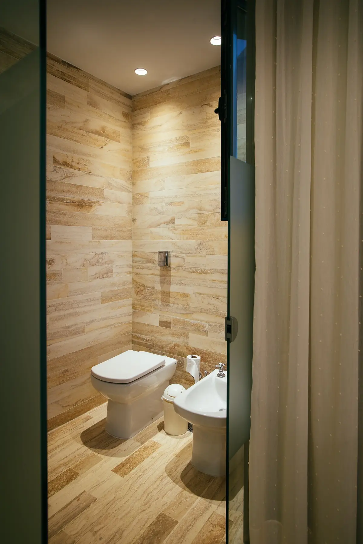 Baño moderno con paredes de piedra símil madera y bidet — proyecto Grand Bell 60, por Mercedes  klappenbach, en City Bell