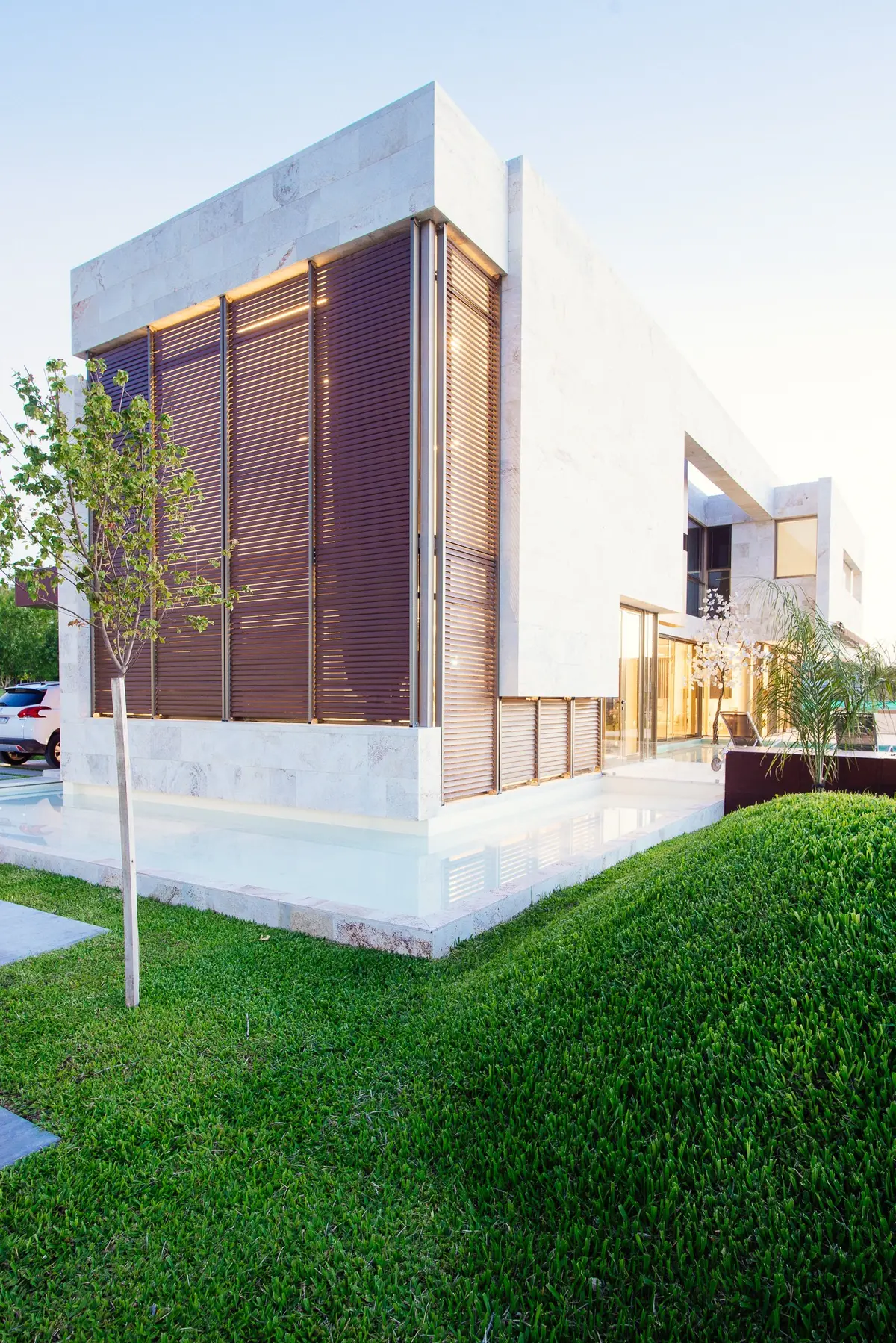 Casa moderna branca de concreto com persianas de madeira e gramado exuberante — projeto Grand Bell 60, por Mercedes  klappenbach, em City Bell