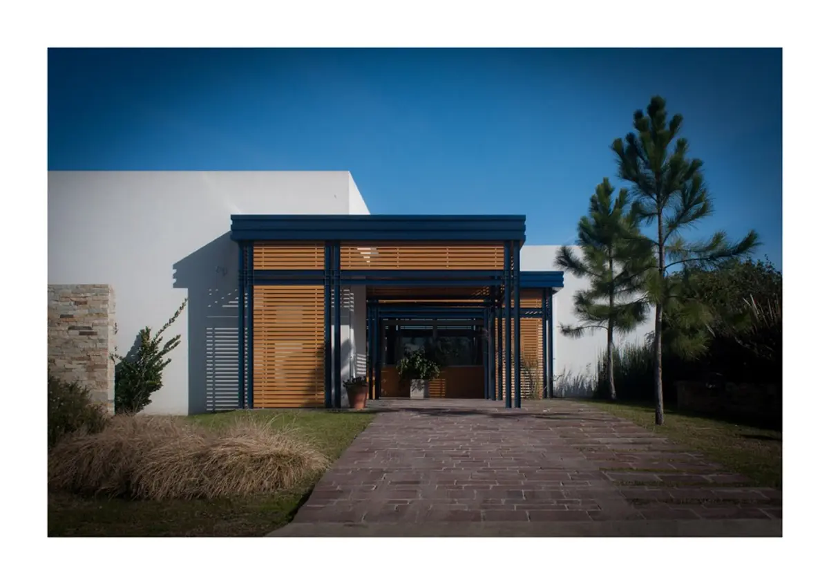Fachada moderna com pergolado de madeira e caminho de tijolos — projeto Los Ceibos 60, por Mercedes  klappenbach, em La Plata