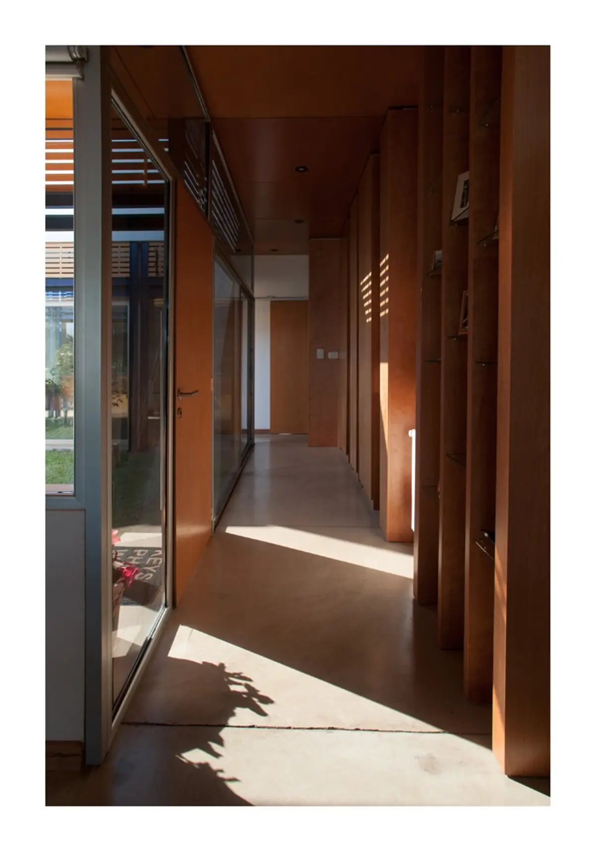 Pasillo moderno con madera natural, concreto y luz solar creando sombras — proyecto Los Ceibos 60, por Mercedes  klappenbach, en La Plata