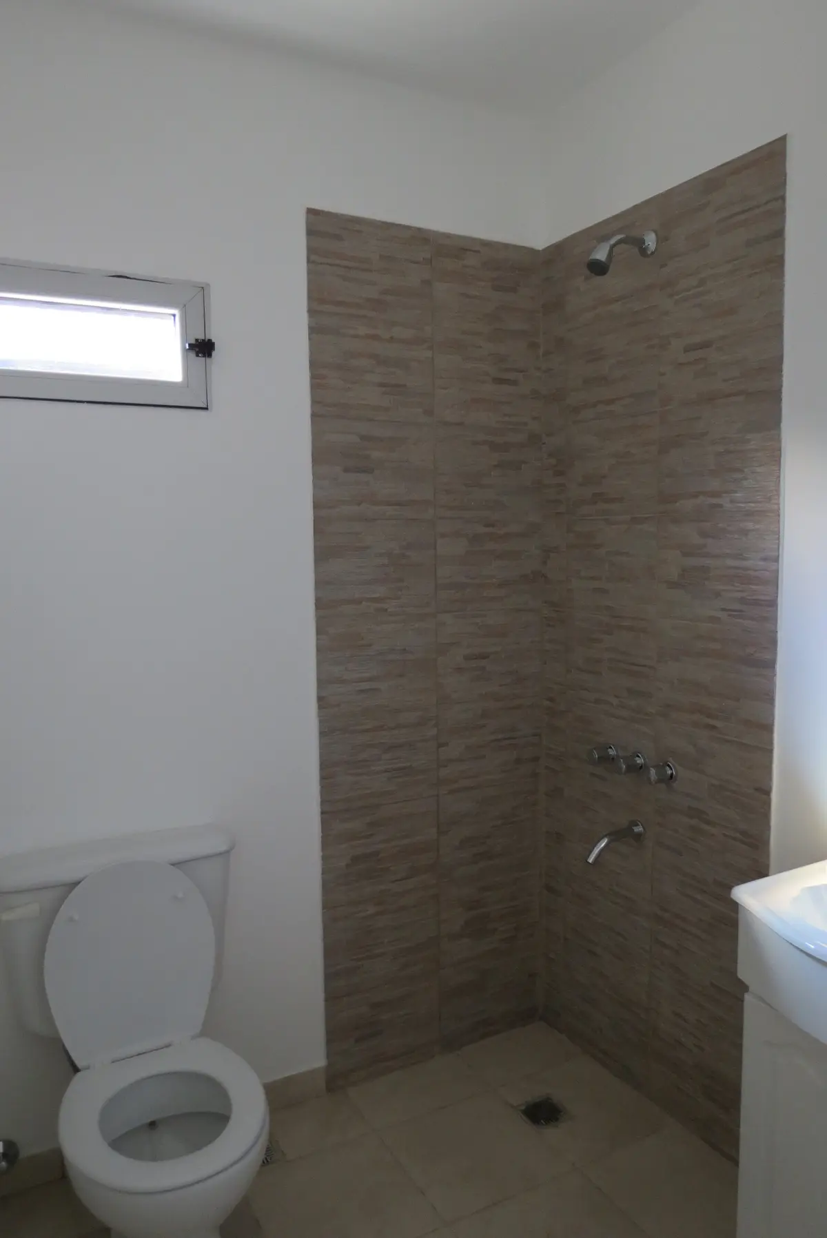 Banheiro moderno com chuveiro de azulejo texturizado e vaso sanitário branco — projeto Ampliación y refacción  San Agustín, por Olivieri Arquitectura, em Tigre