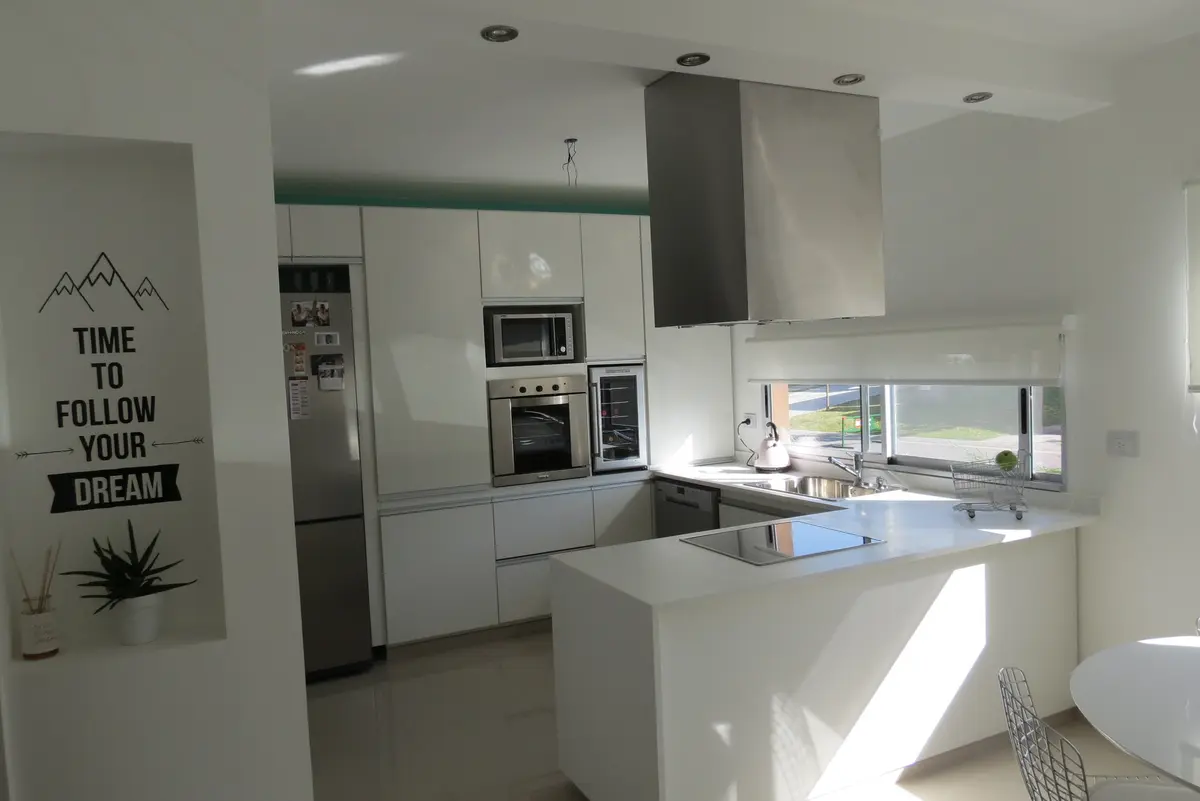 Cocina moderna abierta con isla, luz natural y acabados blancos — proyecto Ampliación y refacción  San Agustín, por Olivieri Arquitectura, en Tigre