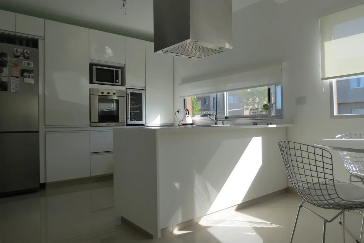 Cocina moderna blanca con isla grande y luz natural — proyecto Ampliación y refacción  San Agustín, por Olivieri Arquitectura, en Tigre