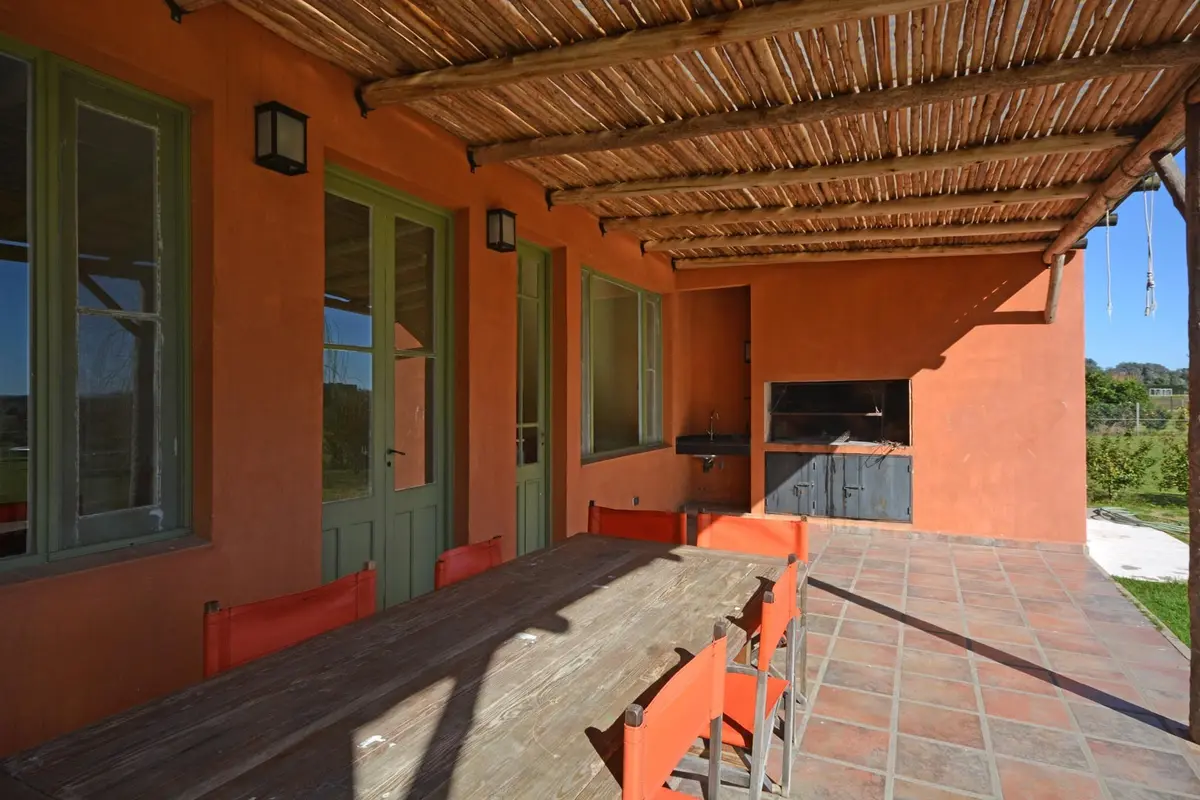 Pátio rústico mediterrâneo com mesa de madeira e cadeiras laranjas — projeto Casa 14, por Estudio Martínez Nespral