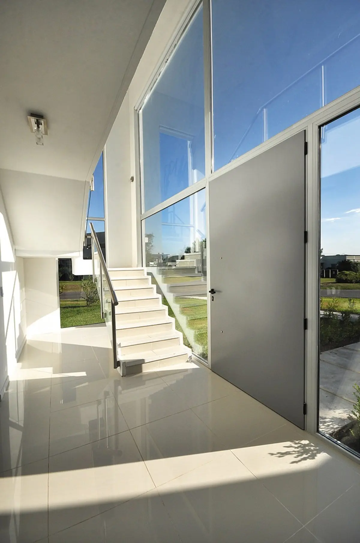 Espaciosa entrada moderna con escalera flotante y ventanales del suelo al techo — proyecto Casa 10, por Estudio Martínez Nespral