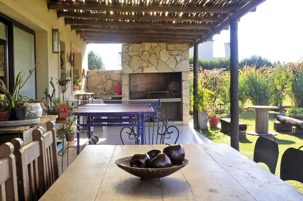 Área de jantar externa rústica com pérgola de madeira e parede de pedra — projeto Casa 9, por Estudio Martínez Nespral
