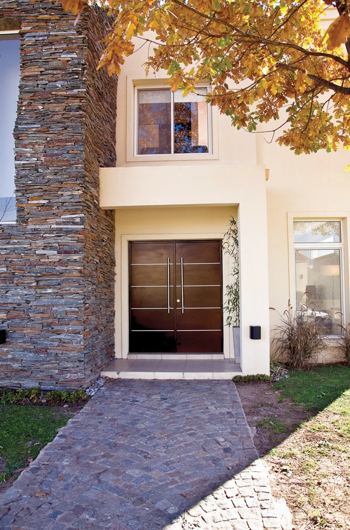 Fachada moderna com porta dupla de madeira, muro de pedra e caminho de paralelepípedos — projeto Casa 7, por Estudio Martínez Nespral