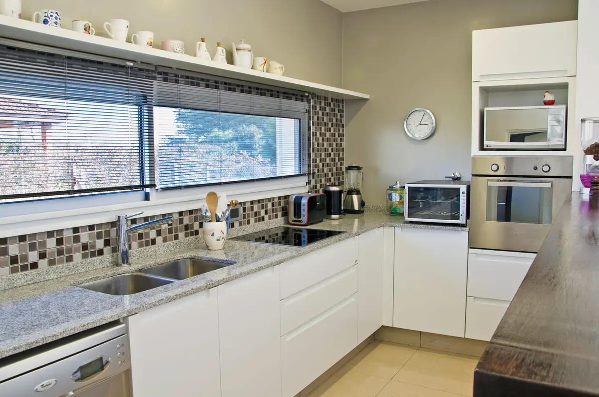 Cozinha moderna com armários brancos, bancada de pedra cinza e backsplash de mosaico — projeto Casa 7, por Estudio Martínez Nespral