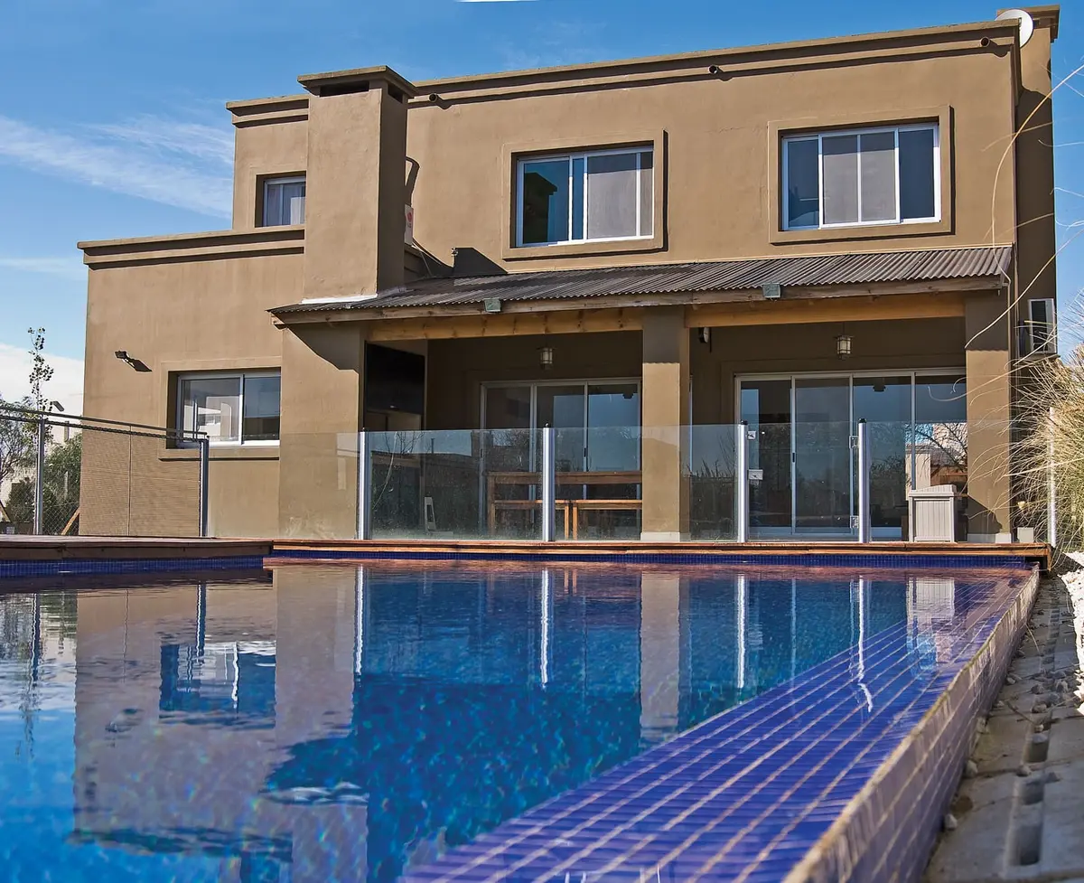 Piscina moderna com borda de cerâmica azul em frente a fachada bege — projeto Casa 5, por Estudio Martínez Nespral