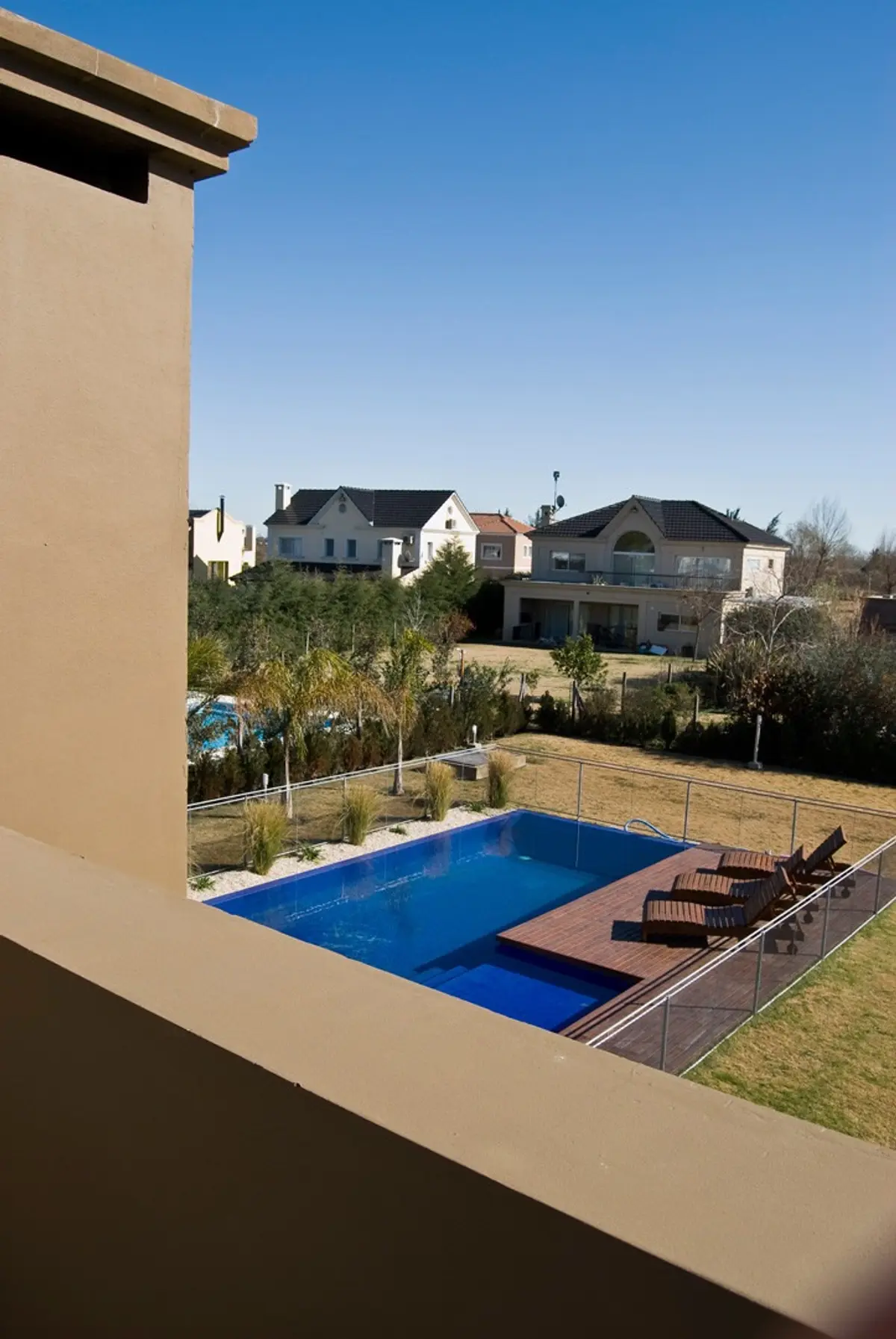 Área de piscina moderna com deck de madeira e casas ao fundo — projeto Casa 5, por Estudio Martínez Nespral