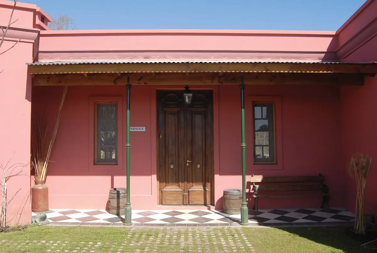 Fachada de casa rural estilo mediterráneo rosa com alpendre e porta de madeira — projeto Casa 2, por Estudio Martínez Nespral