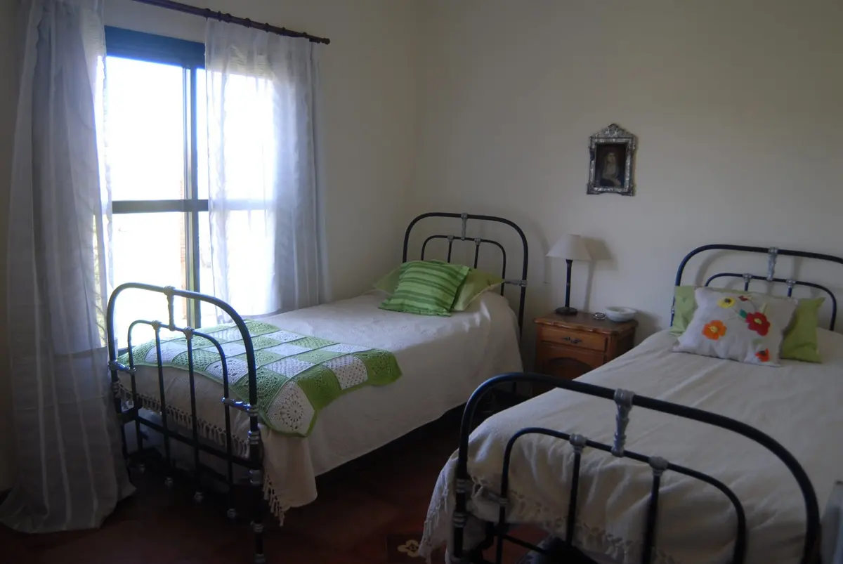 Quarto de fazenda com duas camas, cortinas brancas e luz natural — projeto Casa 2, por Estudio Martínez Nespral