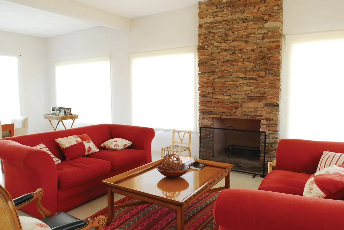 living con chimenea de piedra y sofás rojos — proyecto Casa 1, por Estudio Martínez Nespral