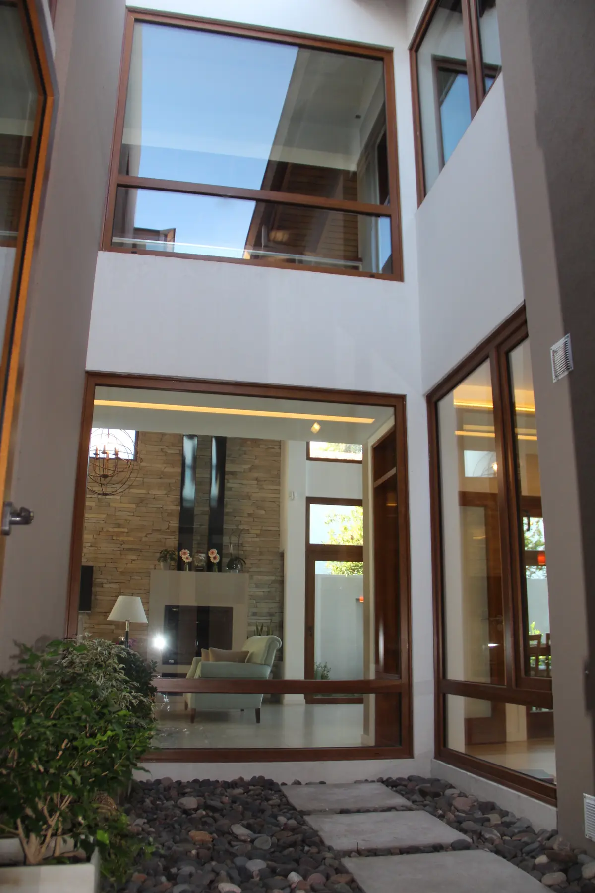 Atrio moderno de doble altura con grandes ventanales y detalles en piedra — proyecto Casa Barrio Parque Luro, por Estudio Arq. Carolina Peruzzo , en Mar del Plata