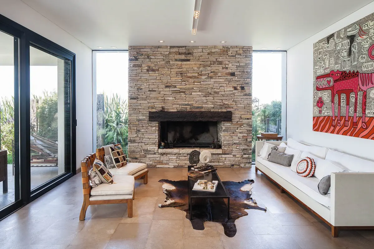 Sala de estar moderna com parede de pedra e lareira, muita luz — projeto Casa DFS, por Estudio Gamboa