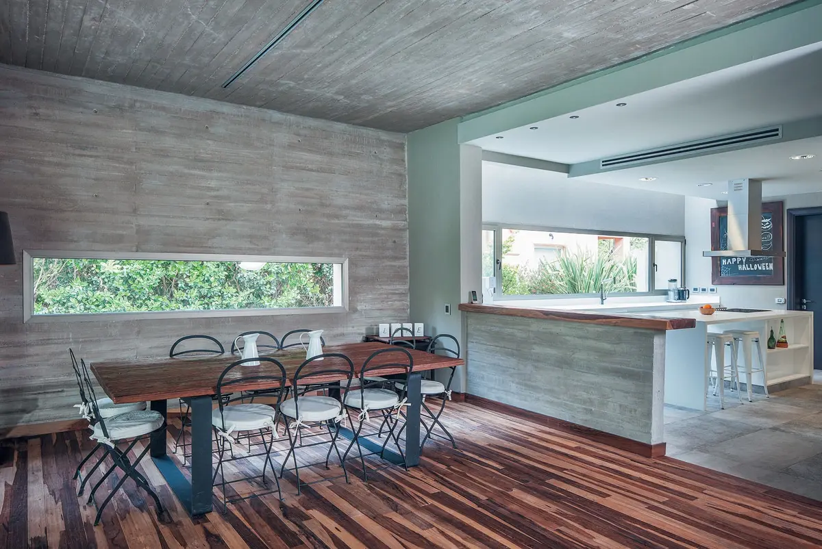 comedor moderno con cocina integrada, paredes de hormigón y madera — proyecto Casa CSZ, por Estudio Gamboa