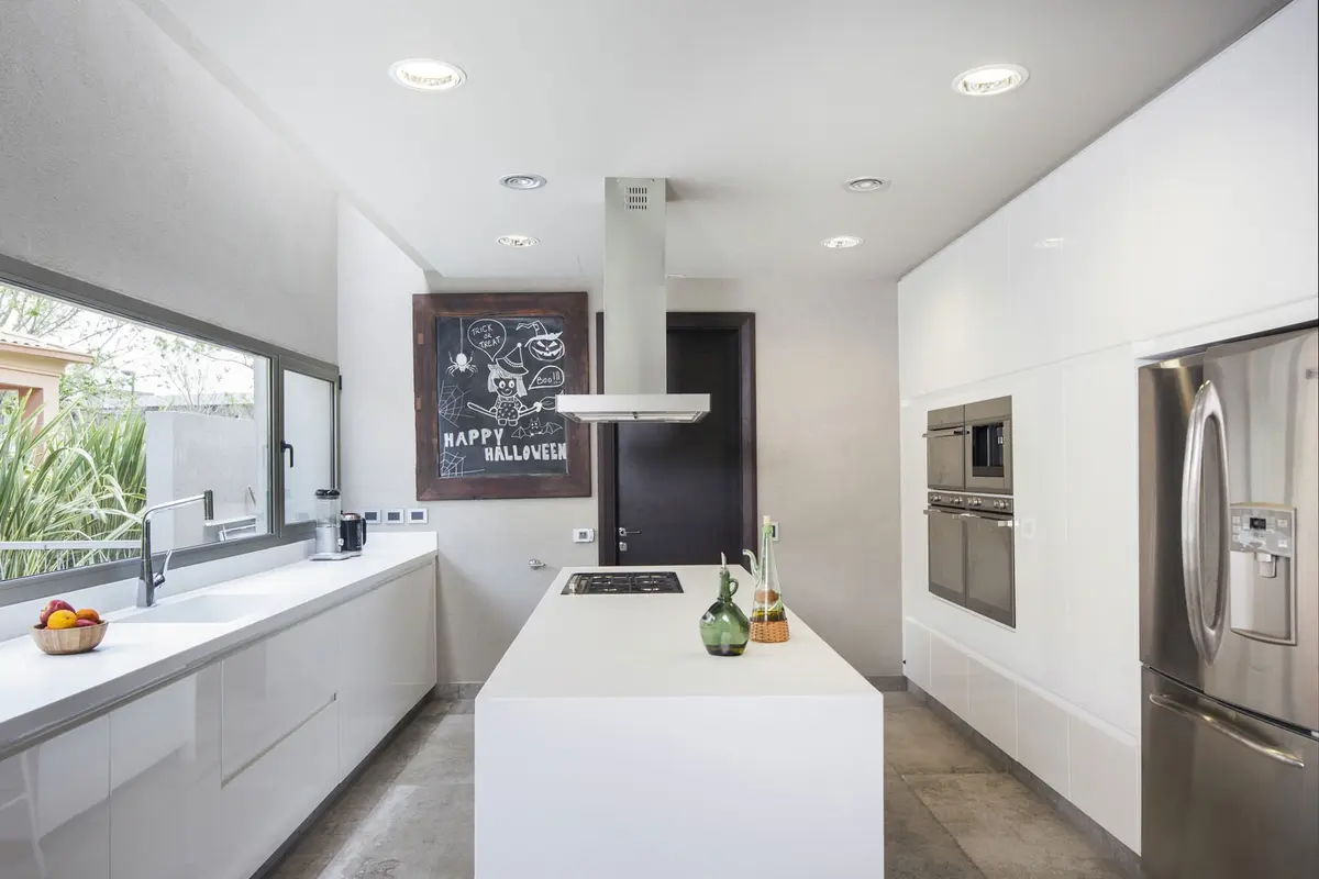 Cocina moderna minimalista con isla blanca y grandes ventanales — proyecto Casa CSZ, por Estudio Gamboa