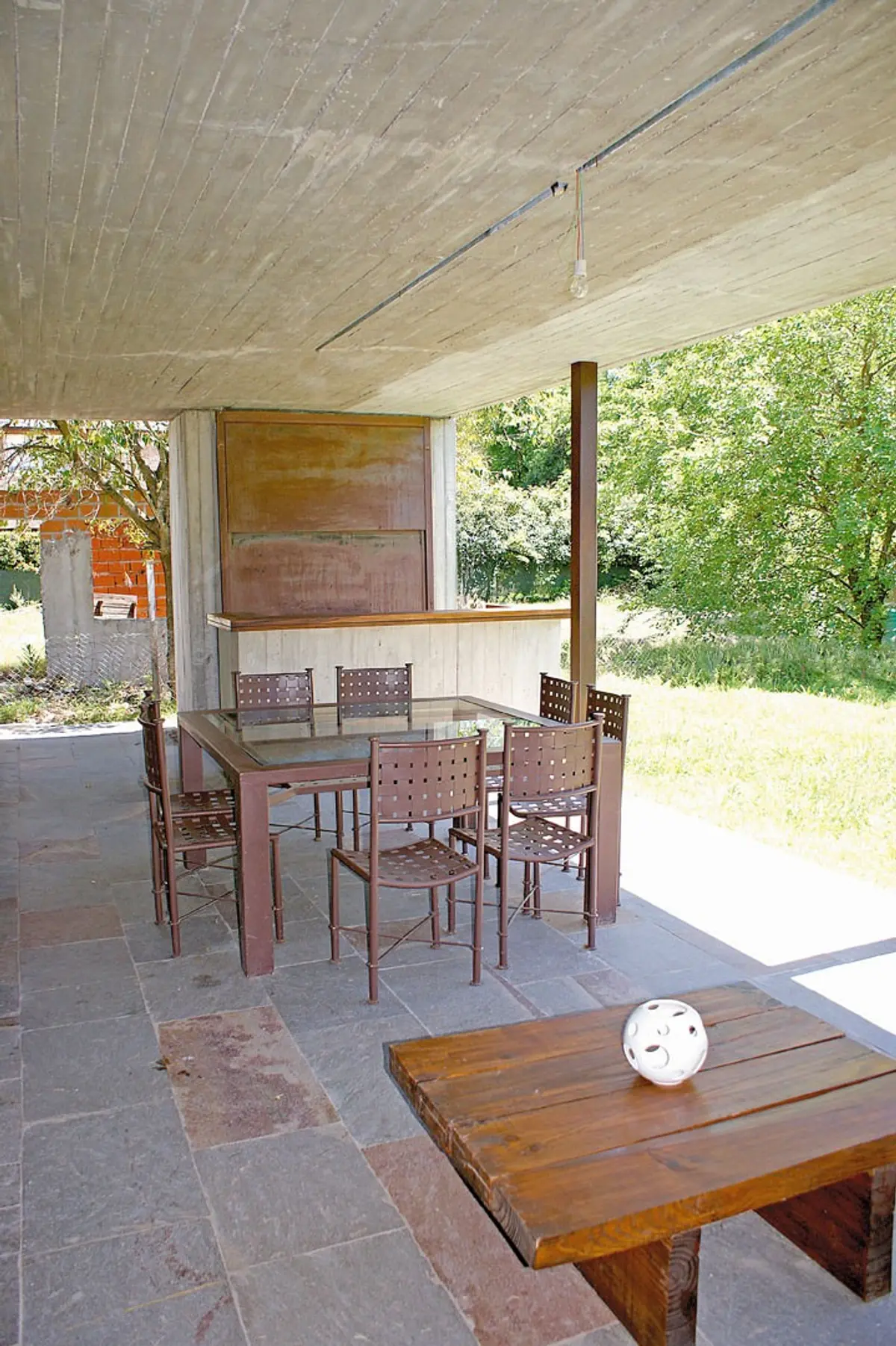 Comedor exterior bajo techo de hormigón con sillas de metal y banco rústico — proyecto Casa CP, por Estudio Gamboa
