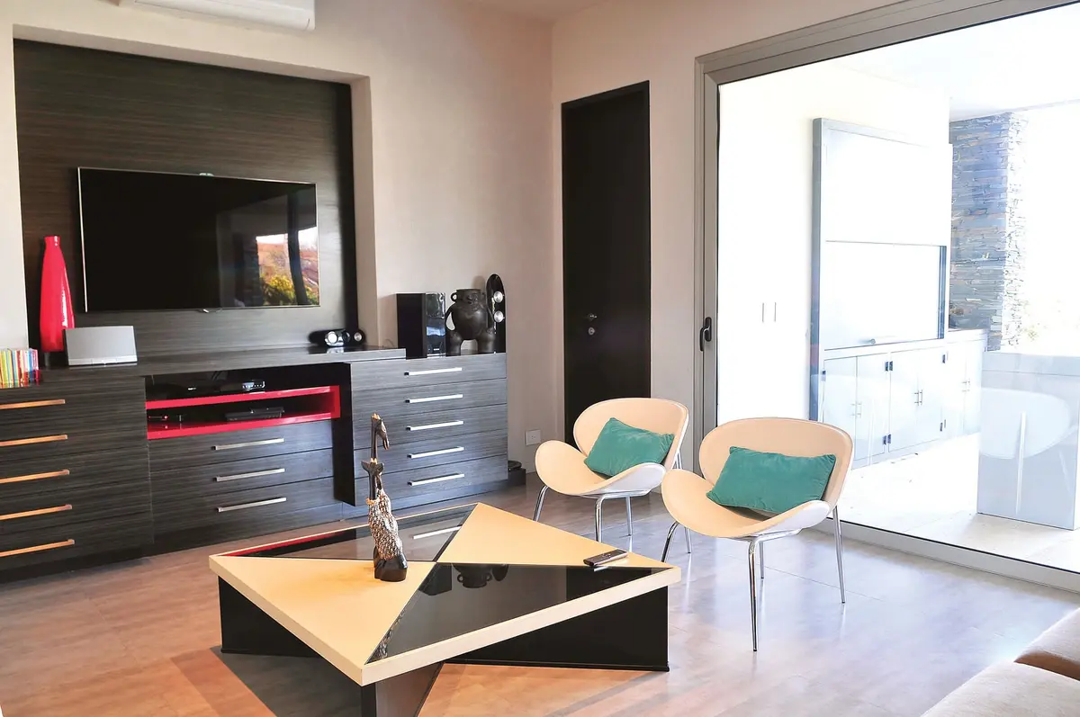 Sala de estar moderna com painéis de madeira escura e móveis geométricos — projeto Casa GGG, por Estudio Gamboa