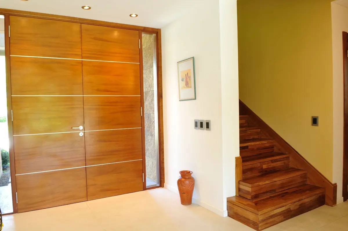 Entrada moderna con puerta de madera y escalera flotante — proyecto Casa GTT, por Estudio Gamboa