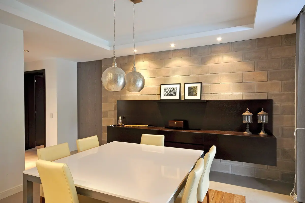 Sala de jantar moderna com mesa branca, cadeiras amarelas e parede de pedra — projeto Casa MMP, por Estudio Gamboa
