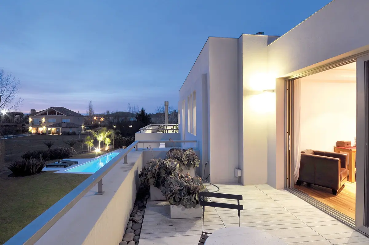 Terraza moderna con sillones de cuero oscuro y vista suburbana al anochecer — proyecto Casa MMP, por Estudio Gamboa