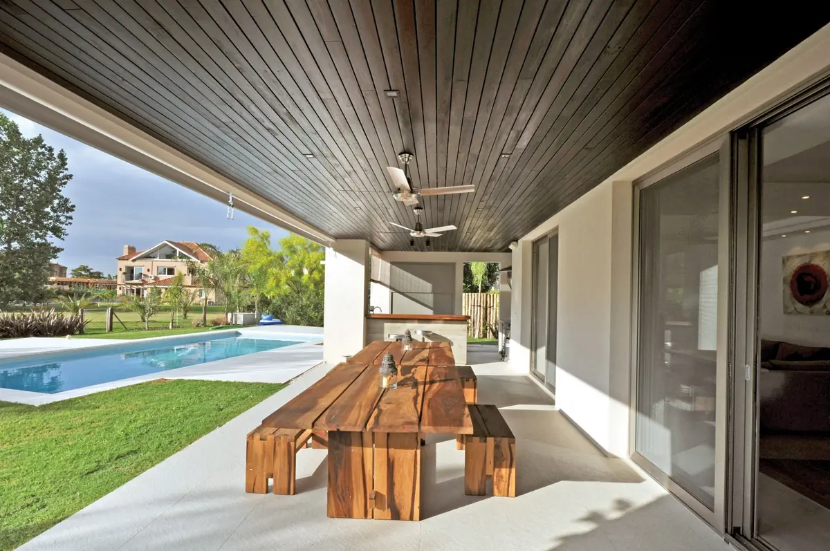 Amplo pátio moderno com mesa rústica de madeira e piscina — projeto Casa MMP, por Estudio Gamboa