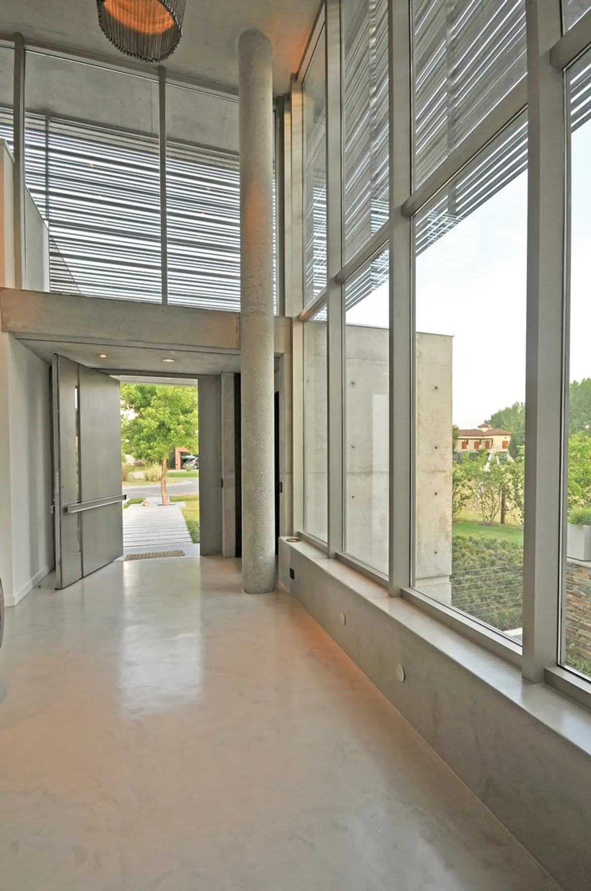 Hall moderno con pisos de cemento y grandes ventanales — proyecto Casa MMP, por Estudio Gamboa