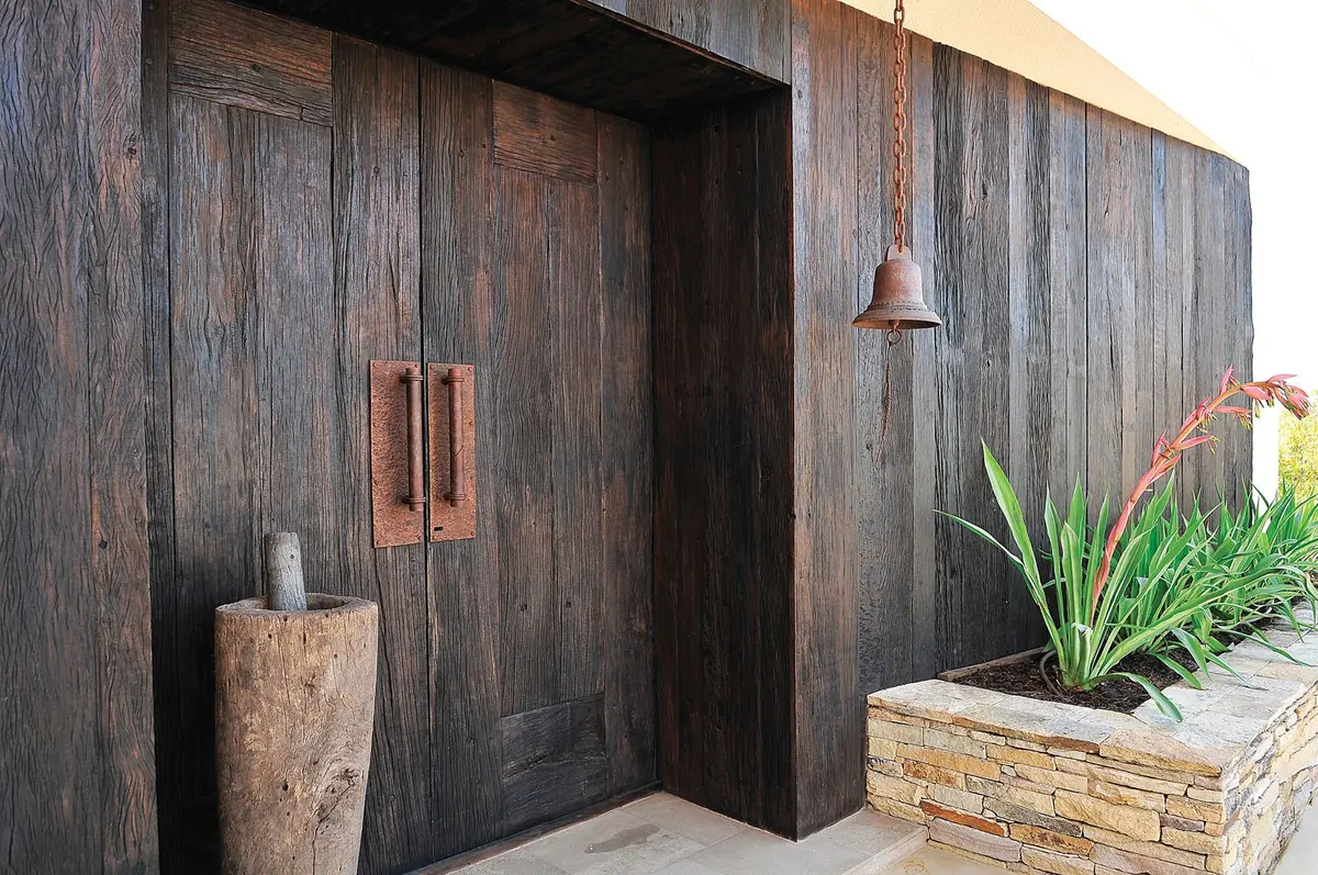 Fachada rústica con puertas de madera oscura y detalles de piedra — proyecto Casa Tigre, por Estudio Gamboa, en Tigre