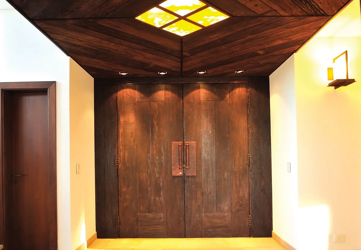 pasillo principal con puertas dobles de madera oscura y lucernario — proyecto Casa Tigre, por Estudio Gamboa, en Tigre