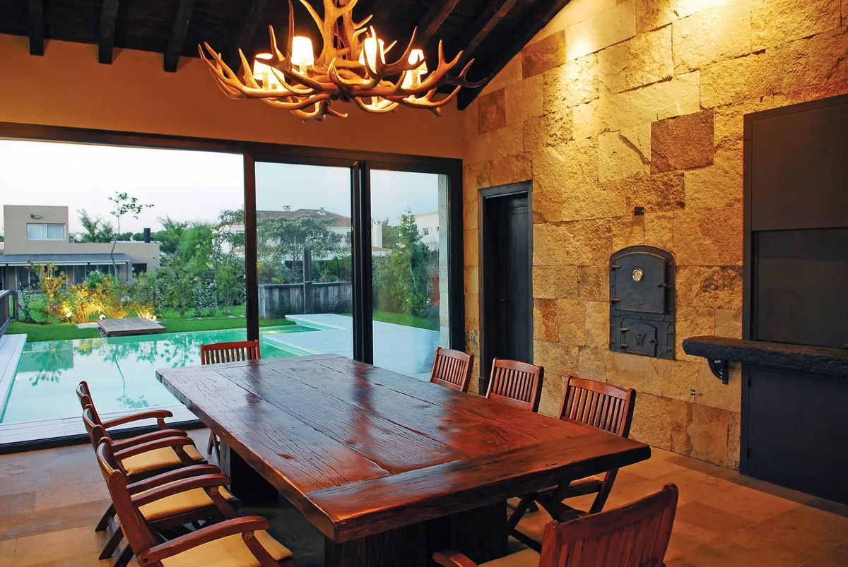 Sala de jantar rústica com mesa de madeira e lustre de chifres — projeto Casa FGR, por Estudio Gamboa