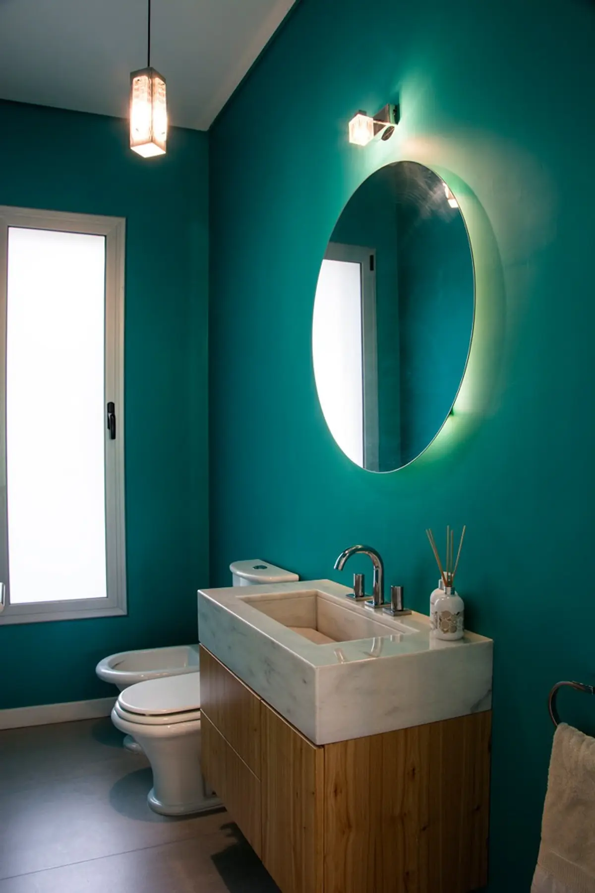 Bano moderno con paredes verde oscuro, mesada madera y espejo circular iluminado — proyecto Casa 18, por Parrado Arquitectura