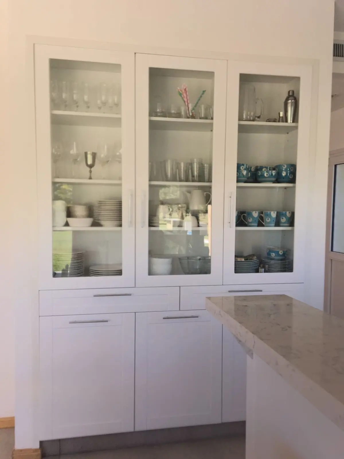 Cocina moderna con alacenas blancas y vidrios, isla de cuarzo — proyecto Vivienda en Miralagos II, por Gabellini-Rey arquitectos, en La Plata