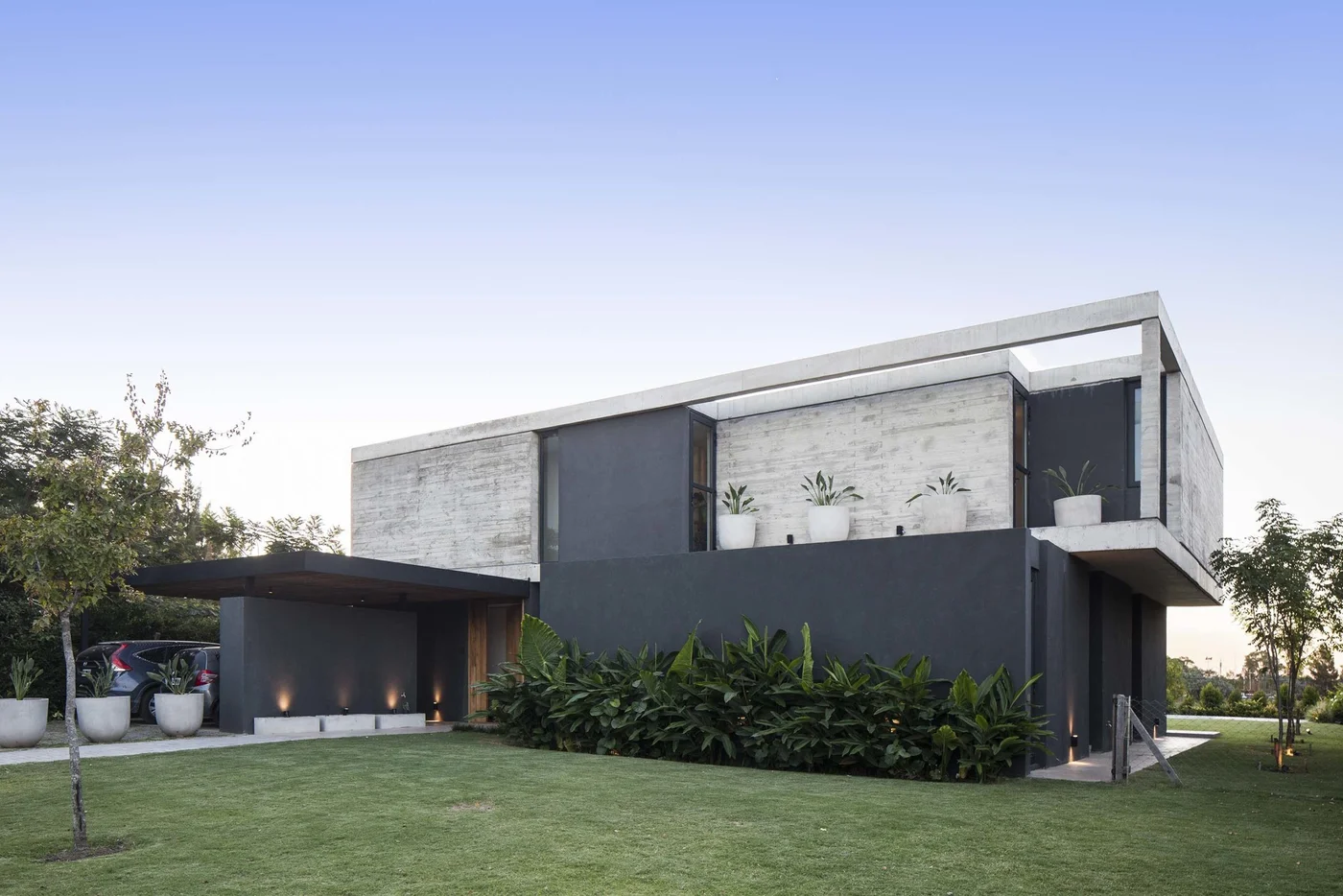 Casa moderna con fachada de hormigón y metal, ventanas amplias y jardín cuidado.