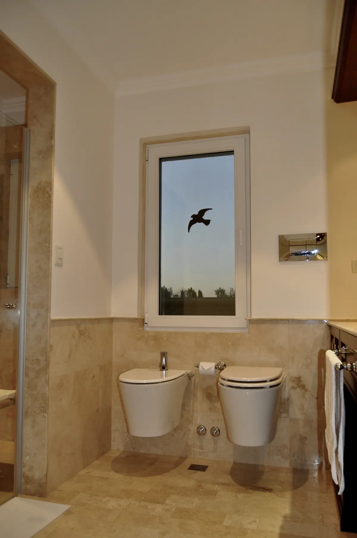 Baño minimalista con dos inodoros blancos y ventanal con vistas al bosque — proyecto Ayres del Pilar, por Marconi Silva Arquitectos, en Pilar