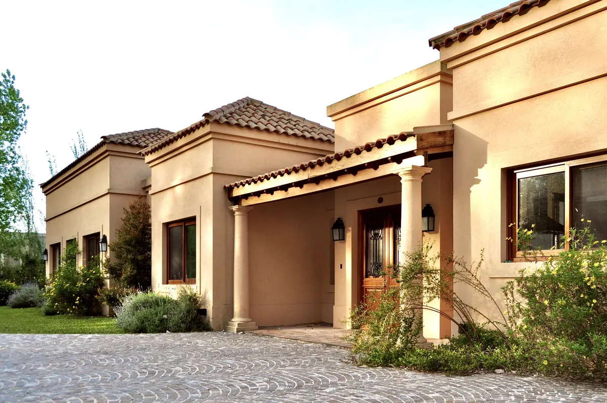Fachada moderna de casa con tonos beige y pergola, entrada con jardineras — proyecto El Solar de Capilla, por Marconi Silva Arquitectos, en Capilla del Señor