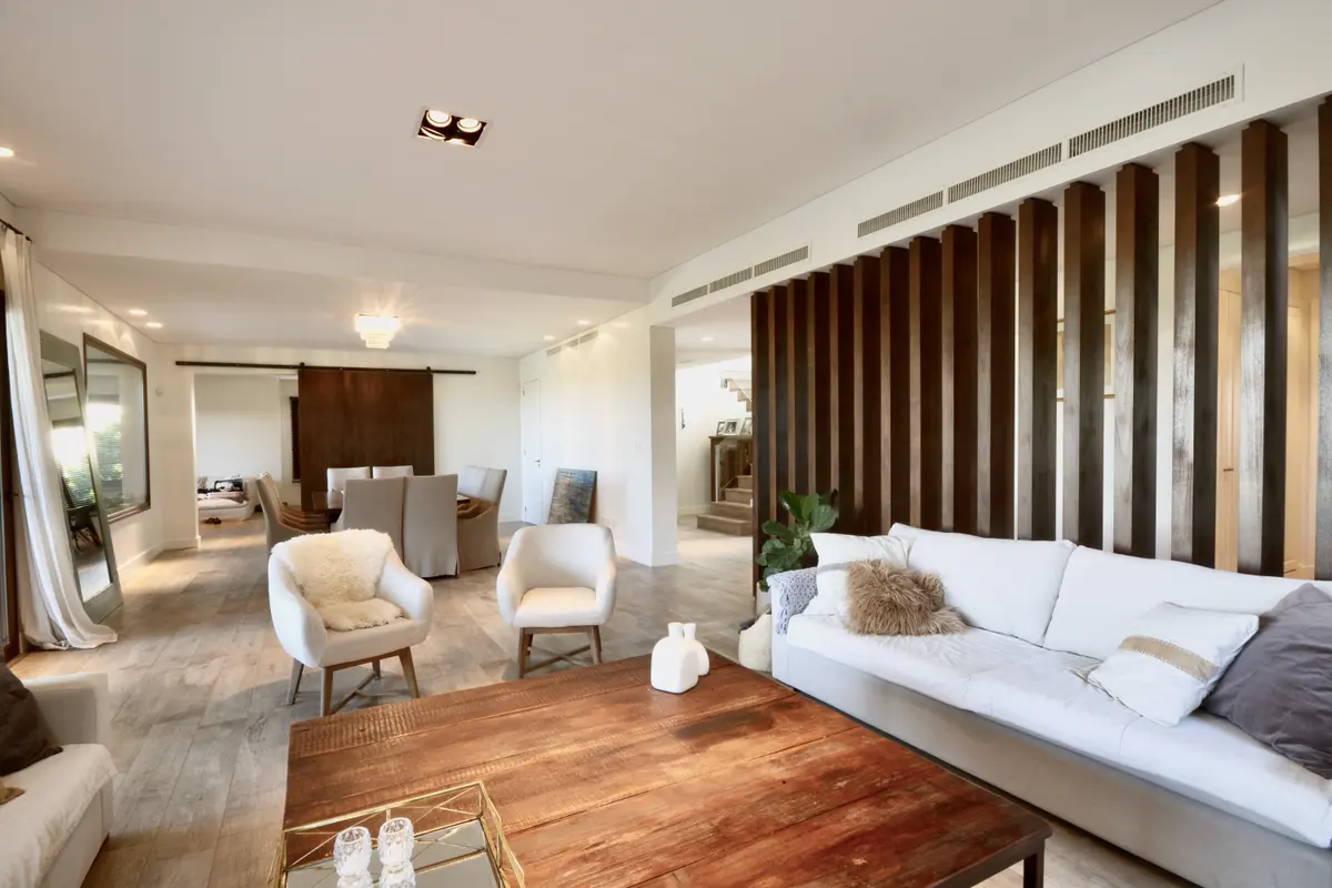 Suite moderna con cama blanca, sillones crema y divisor de madera vertical — proyecto Golf Club Nordelta, por Marconi Silva Arquitectos, en Nordelta