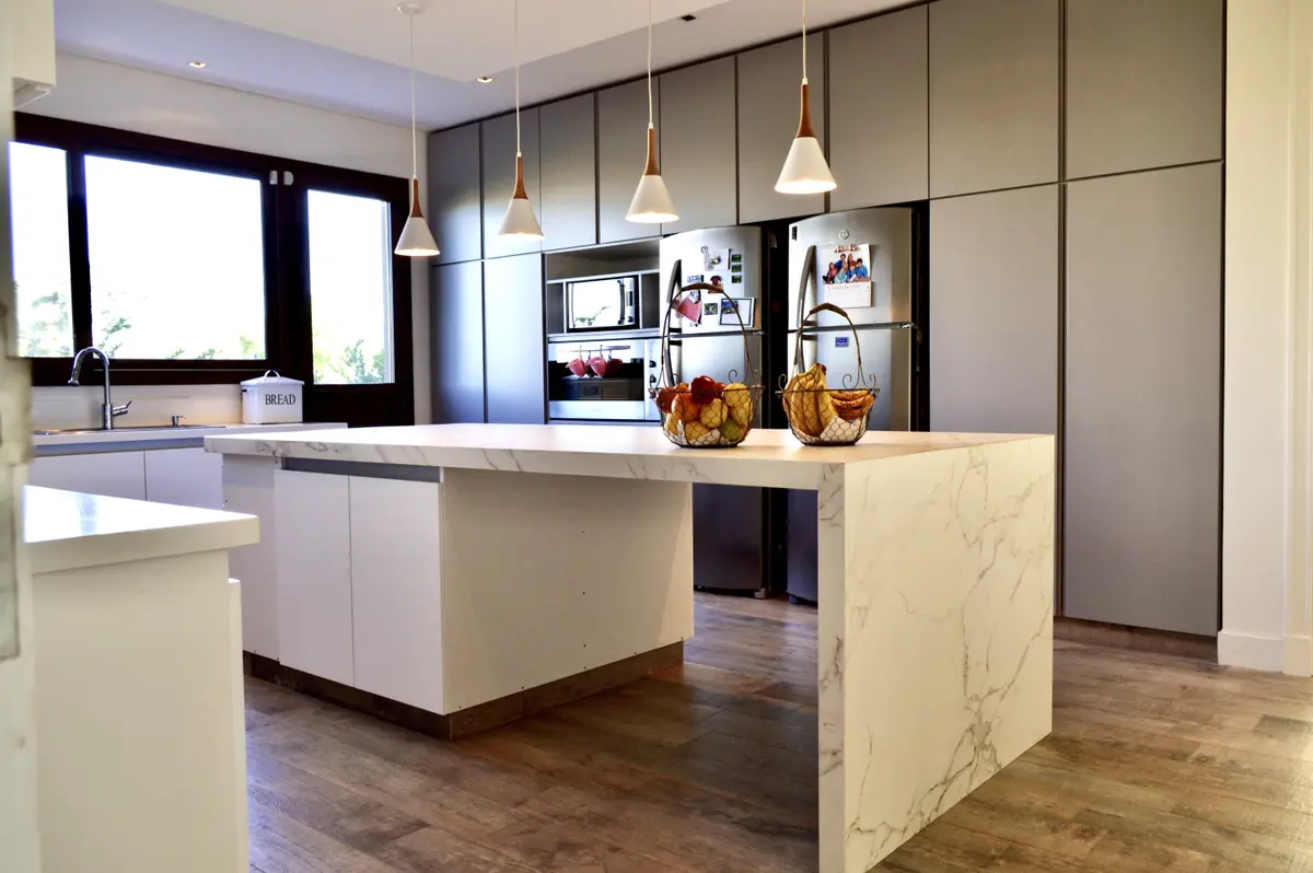 Cocina moderna con isla de mármol y muebles blancos — proyecto Golf Club Nordelta, por Marconi Silva Arquitectos, en Nordelta