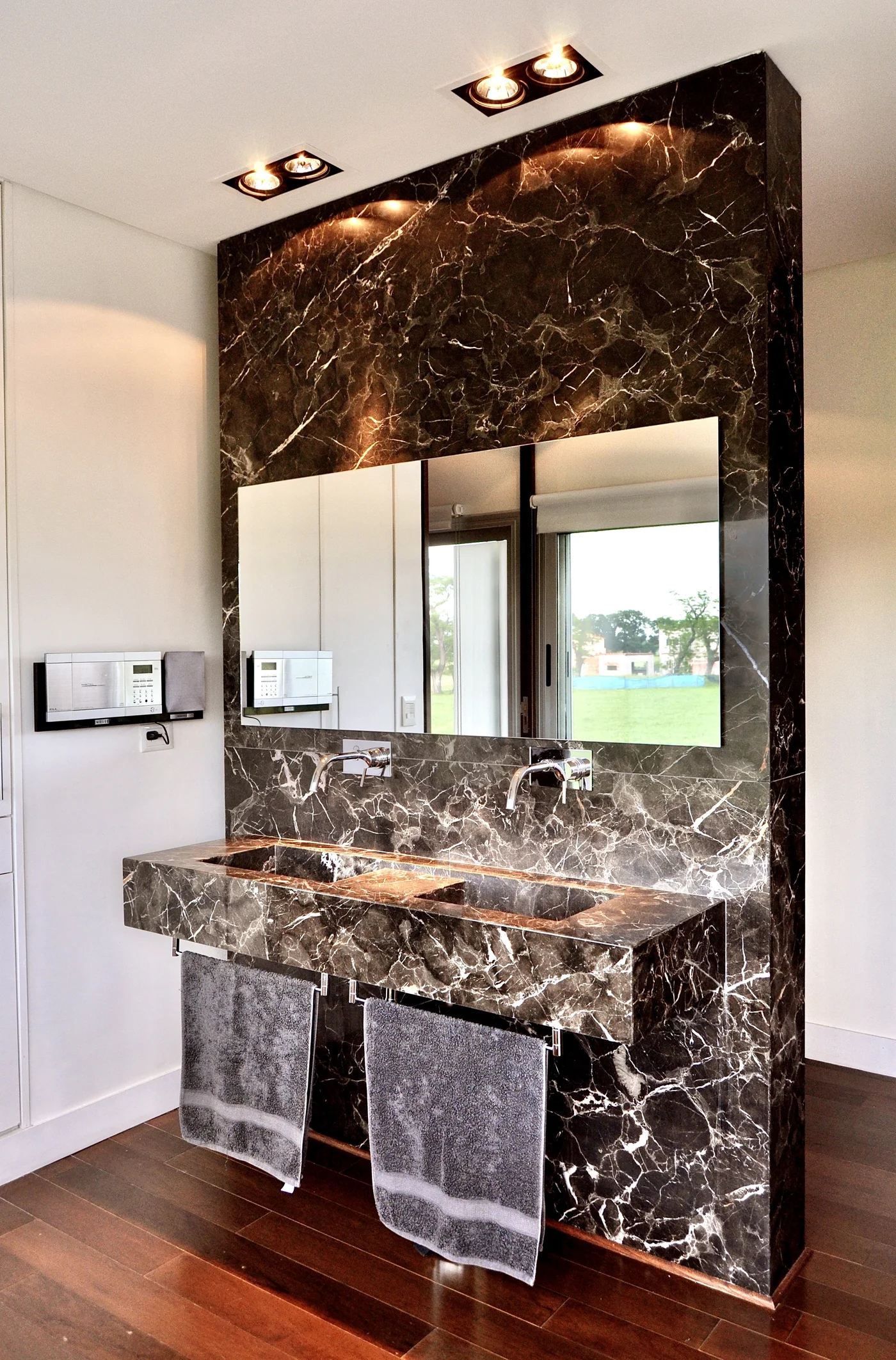 Baño minimalista con mesada marmol negro y espejo grande iluminado