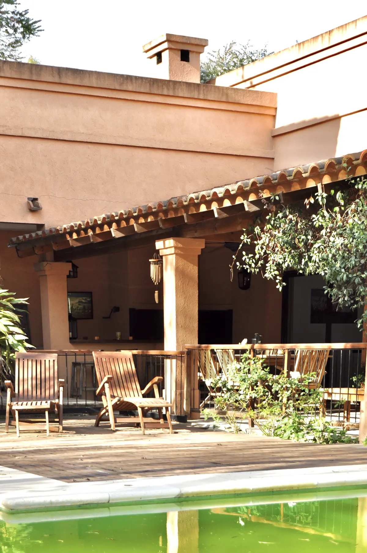 Patio con pileta verde, pergola madera y deck frente a casa terracota — proyecto La Retama, por Marconi Silva Arquitectos, en Manzanares