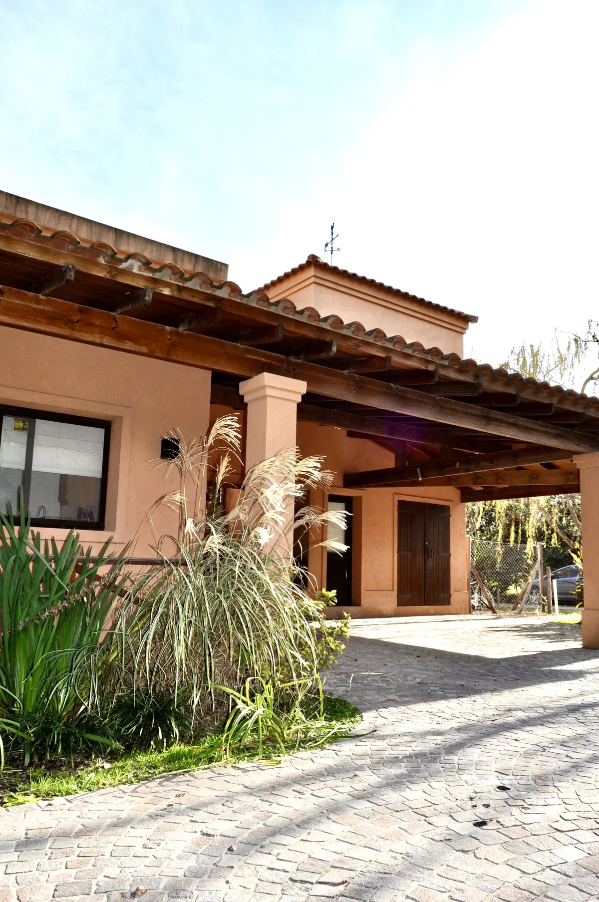 Fachada de casa con arcadas, techo de tejas y jardin lateral — proyecto La Retama, por Marconi Silva Arquitectos, en Manzanares