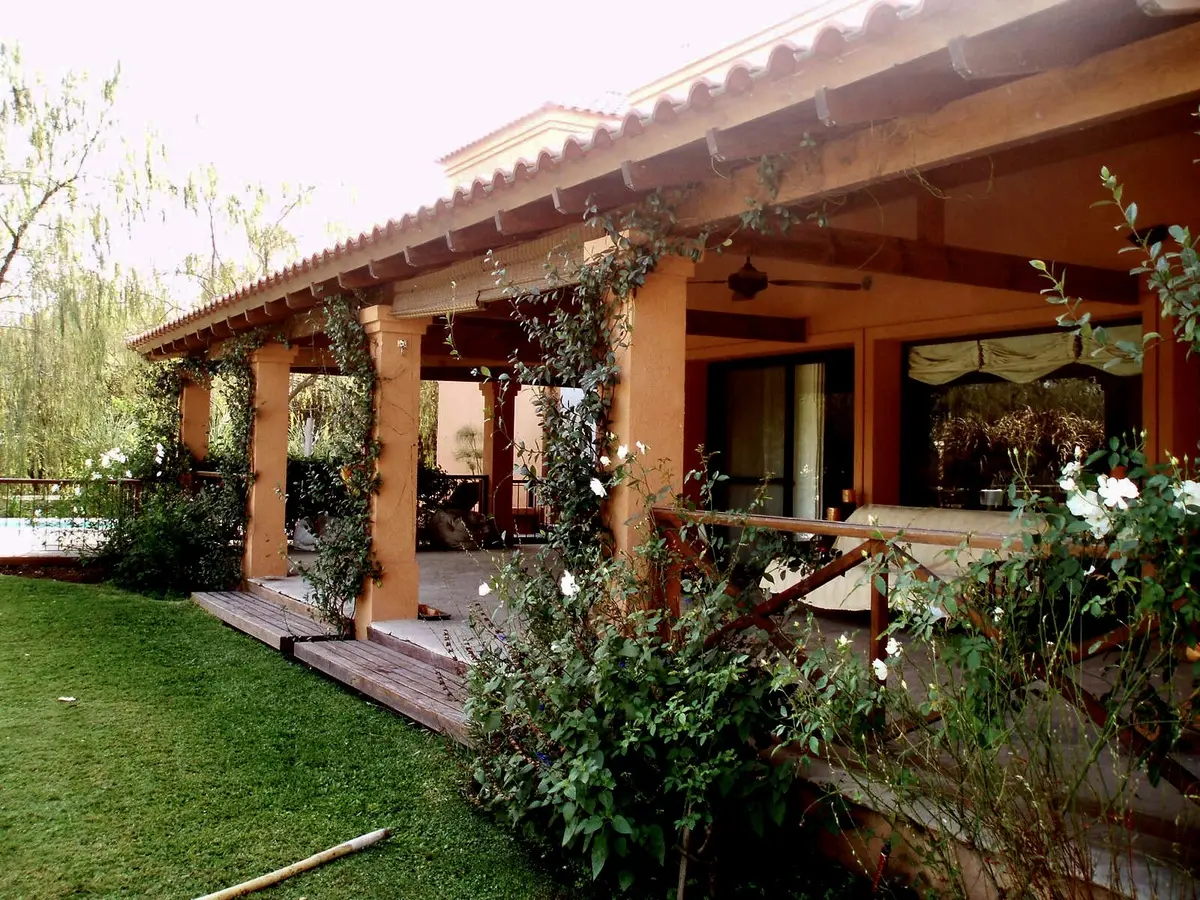Galería de madera terracota con enredaderas verdes y jardín frondoso — proyecto La Retama, por Marconi Silva Arquitectos, en Manzanares
