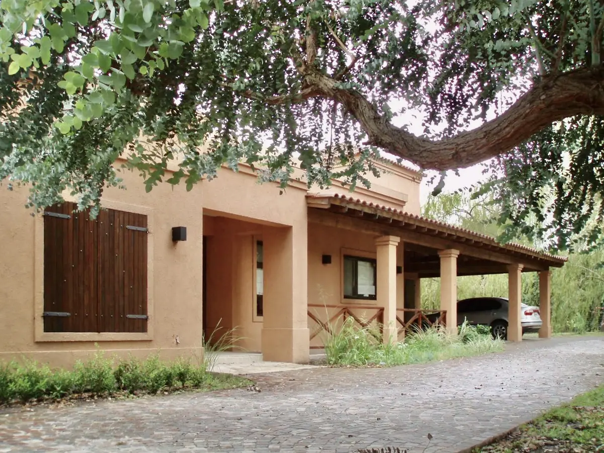 Casa de campo con fachada terracota, porche cubierto y frondoso árbol — proyecto La Retama, por Marconi Silva Arquitectos, en Manzanares