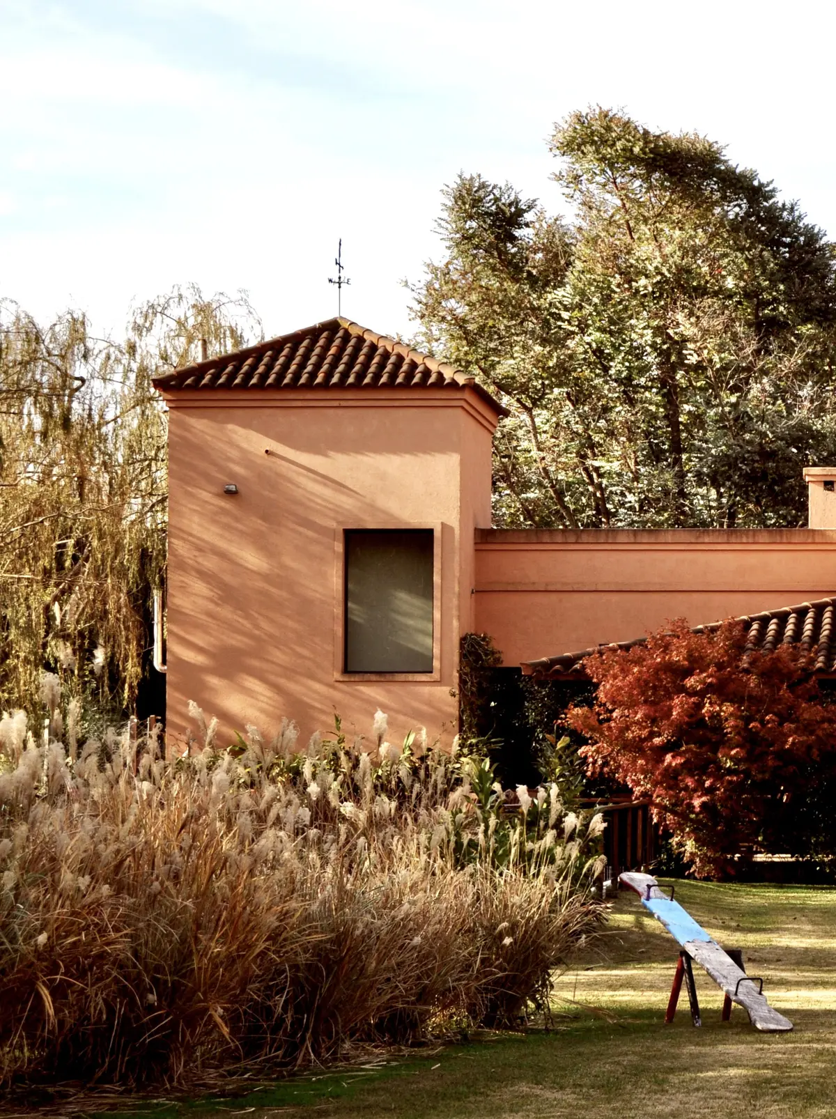 Torre de ladrillo terracota en jardín con plantas y árboles — proyecto La Retama, por Marconi Silva Arquitectos, en Manzanares
