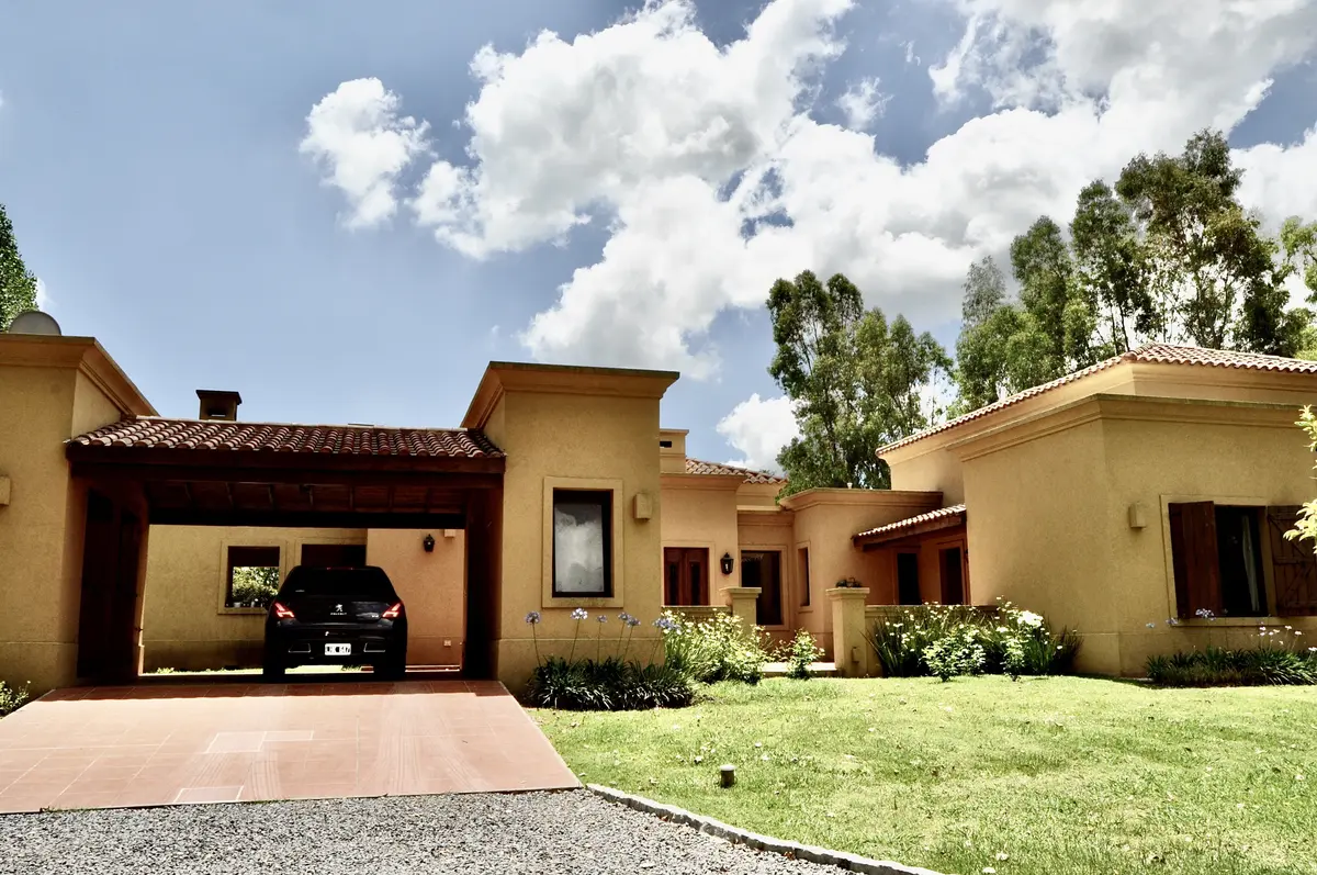 Fachada contemporánea en tonos tierra con garaje y jardín frondoso — proyecto La Retama 2, por Marconi Silva Arquitectos, en Manzanares