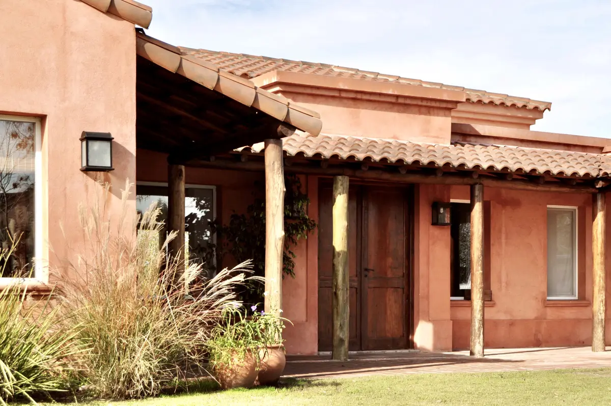 Fachada de casa rural terracota con galería techada y jardín frontal — proyecto San Francisco 1, por Marconi Silva Arquitectos, en Manzanares