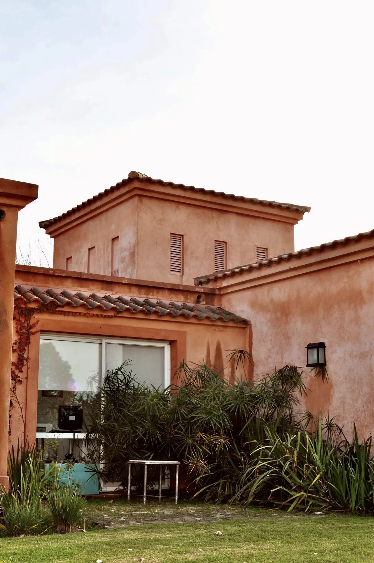 Patio con plantas, césped y fachada terracota con ventanal grande — proyecto San Francisco 1, por Marconi Silva Arquitectos, en Manzanares